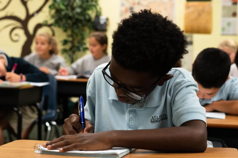 Student writing with a pen at a classroom desk at ACA